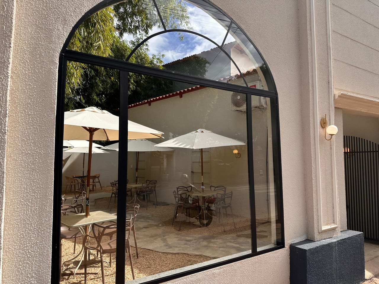 Janela arqueada da cafeteria com vista para o pátio externo com mesas e guarda-sóis em Uruaçu