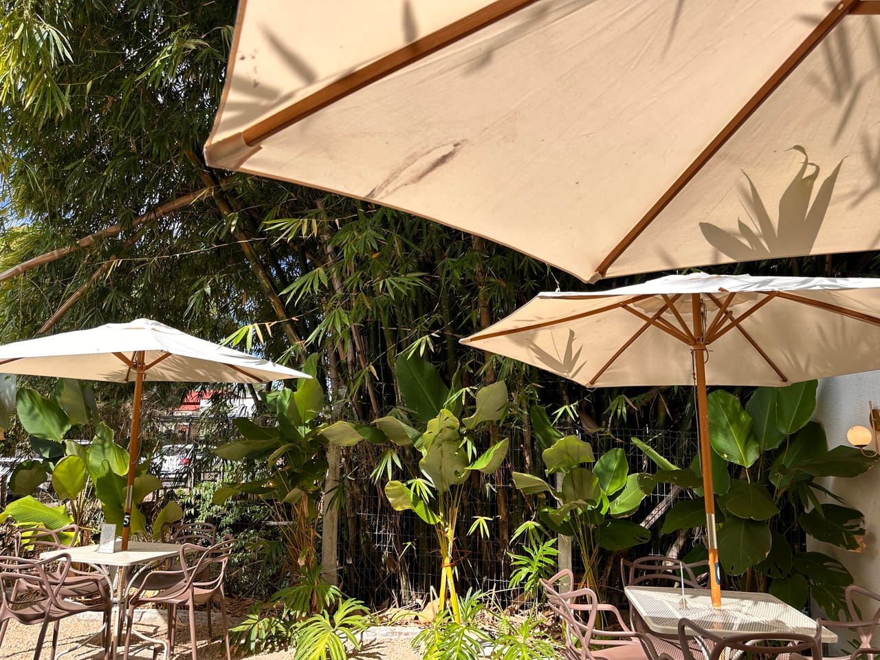Área externa da cafeteria Angels Coffee Br com guarda-sóis bege, mesas e plantas, Uruaçu-GO