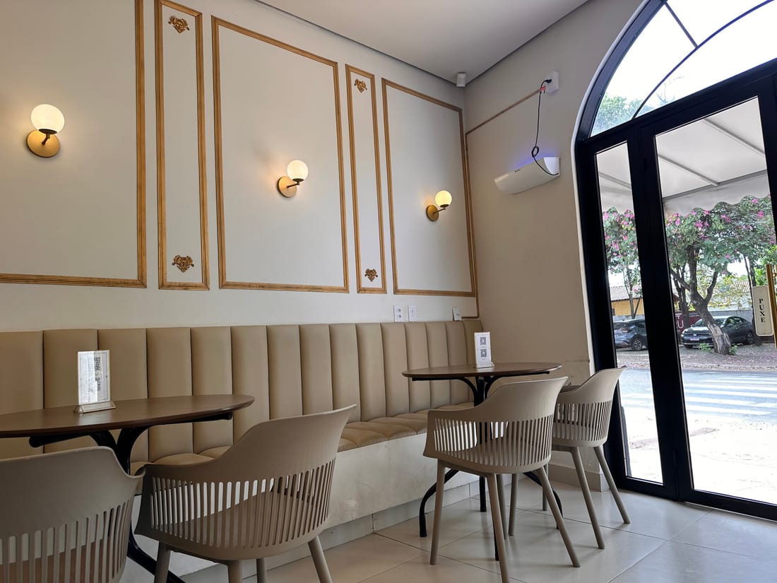 Salão interno da cafeteria Angels Coffee Br em Uruaçu, com banco estofado, arandelas douradas e mesas